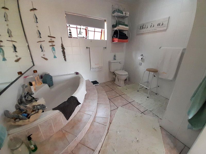A functional bathroom featuring a raised corner bathtub with tiled steps, ceramic floor tiles, and a wall-mounted toilet.