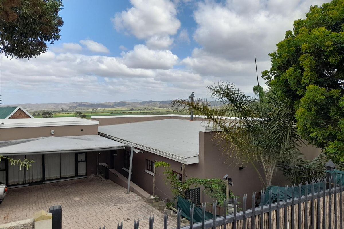 Rear view of the property featuring a paved driveway, covered patio area, and metal roofing, set against a scenic landscape backdrop.