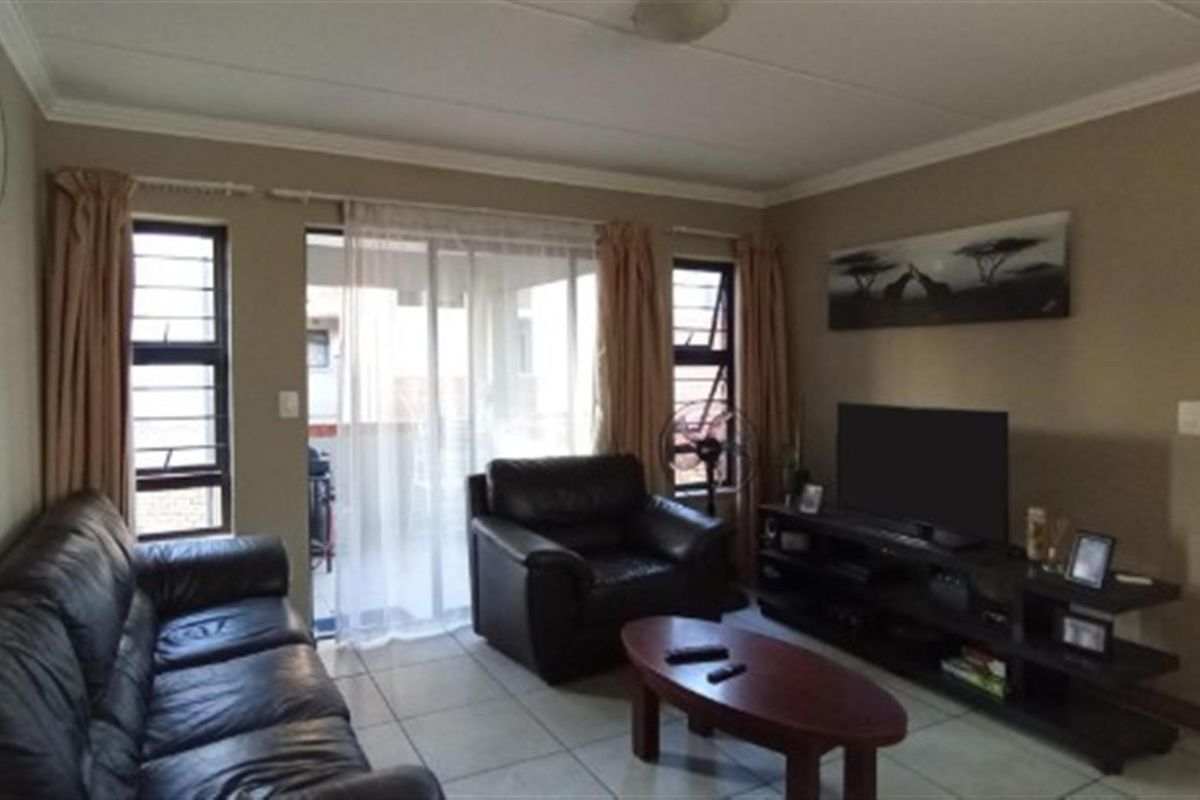 A comfortable living room featuring tiled flooring, large windows, and sliding glass doors that provide access to an outdoor patio area.