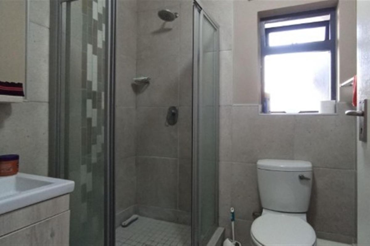 A functional bathroom featuring a glass-enclosed shower, a modern vanity basin, and a standard toilet with neutral wall tiling.