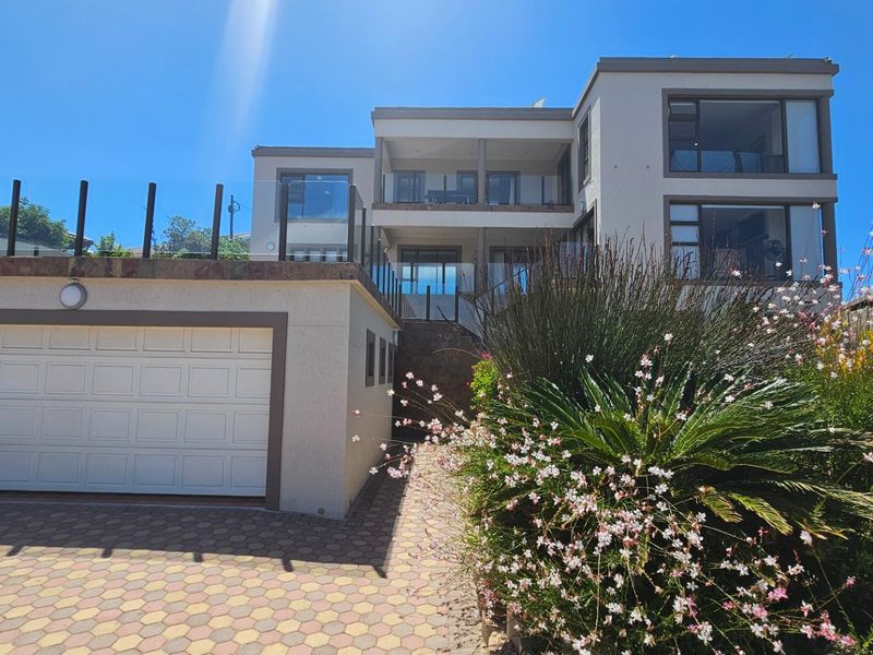 A modern multi-level residential property featuring a paved driveway, double garage, and glass balustrades on the upper balconies.
