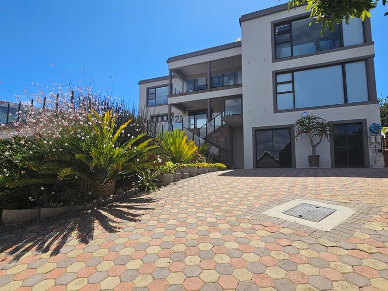A modern multi-level residential property featuring a paved driveway, glass balustrades, and large windows, showcasing a well-maintained exterior facade.