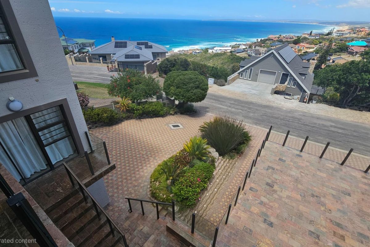 Elevated aerial view of the property exterior, featuring a paved driveway, landscaped garden, and coastal ocean views.