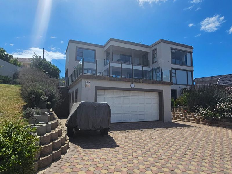 Front elevation of a multi-level house featuring a double garage, paved driveway, and an upper-level balcony with glass balustrades.