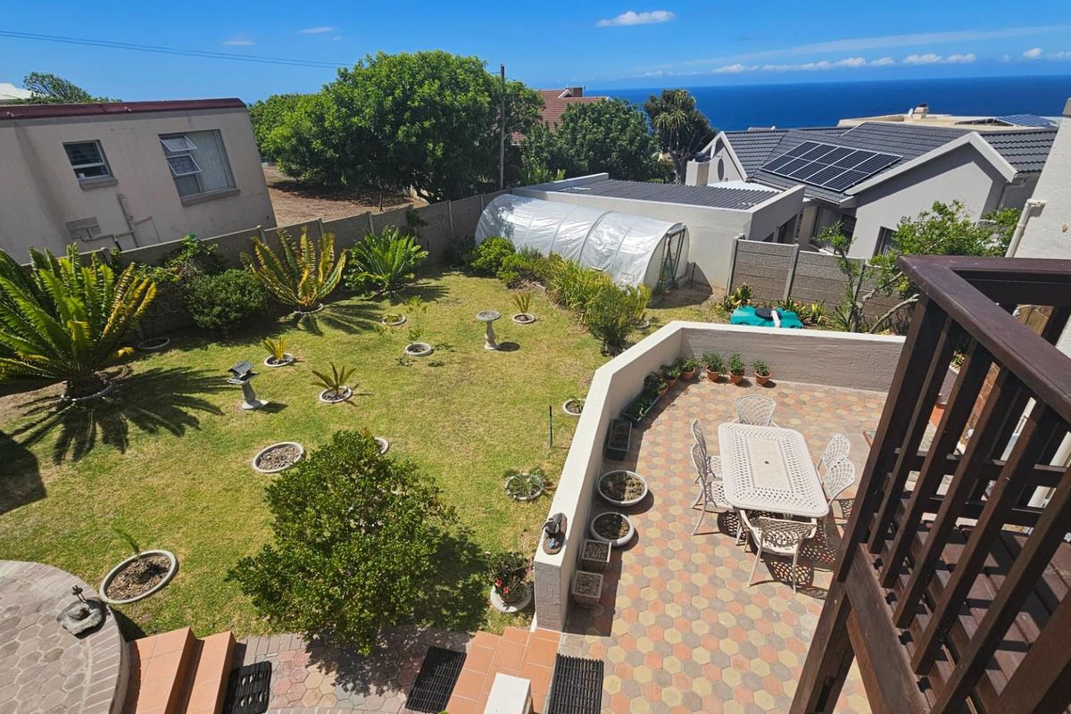 Elevated view of a rear garden featuring a paved patio area, lawn, and boundary walls with a distant ocean view.