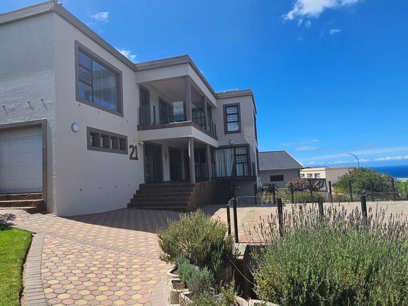 A modern multi-story residential property featuring a paved driveway, integrated garage, and upper-level balconies with glass balustrades, offering a clear view of the surroundings.