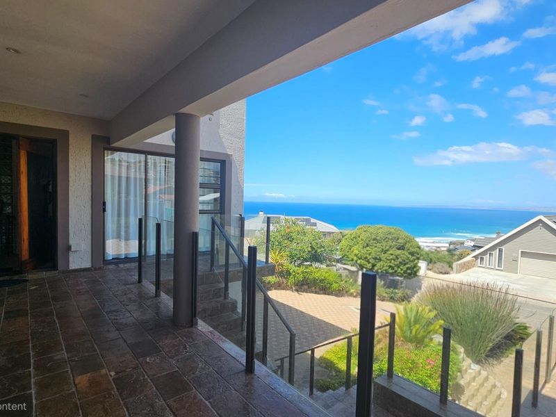 Spacious covered balcony featuring tiled flooring, a modern glass balustrade, and expansive elevated ocean views.