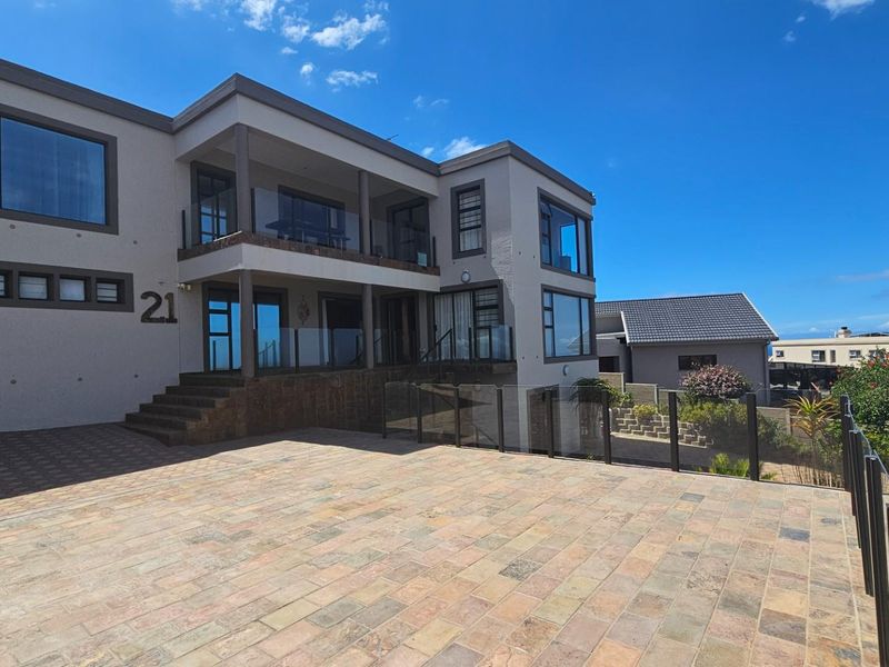 Modern multi-level residential property featuring a paved driveway, glass balustrades, and a covered balcony with contemporary architectural finishes.