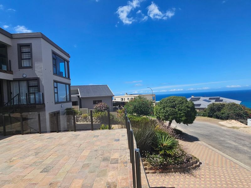 Spacious elevated patio featuring stone tile flooring and a modern glass balustrade, offering expansive coastal and ocean views.
