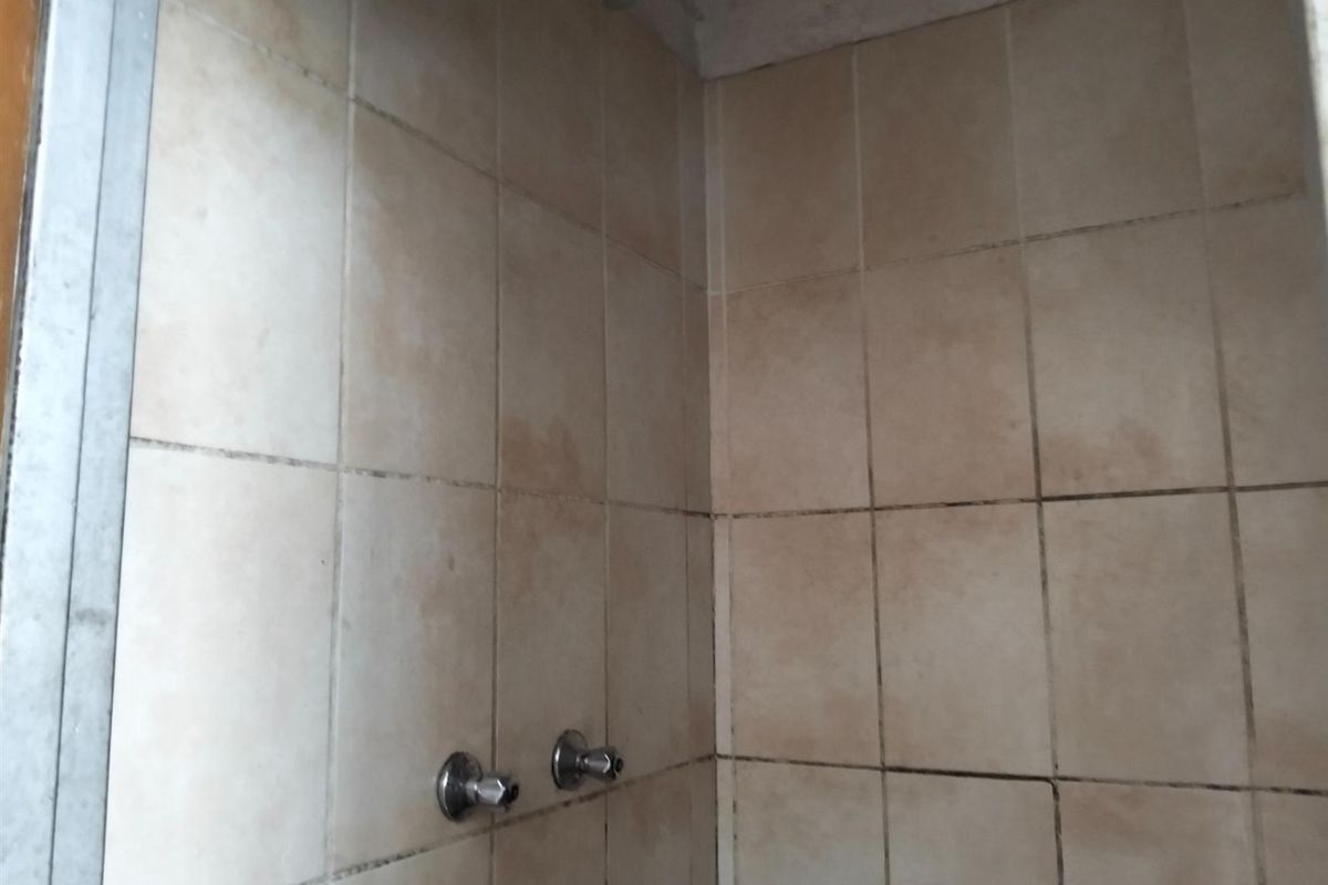 A shower enclosure featuring dated wall tiling and basic plumbing fixtures, showing significant signs of wear and surface staining.