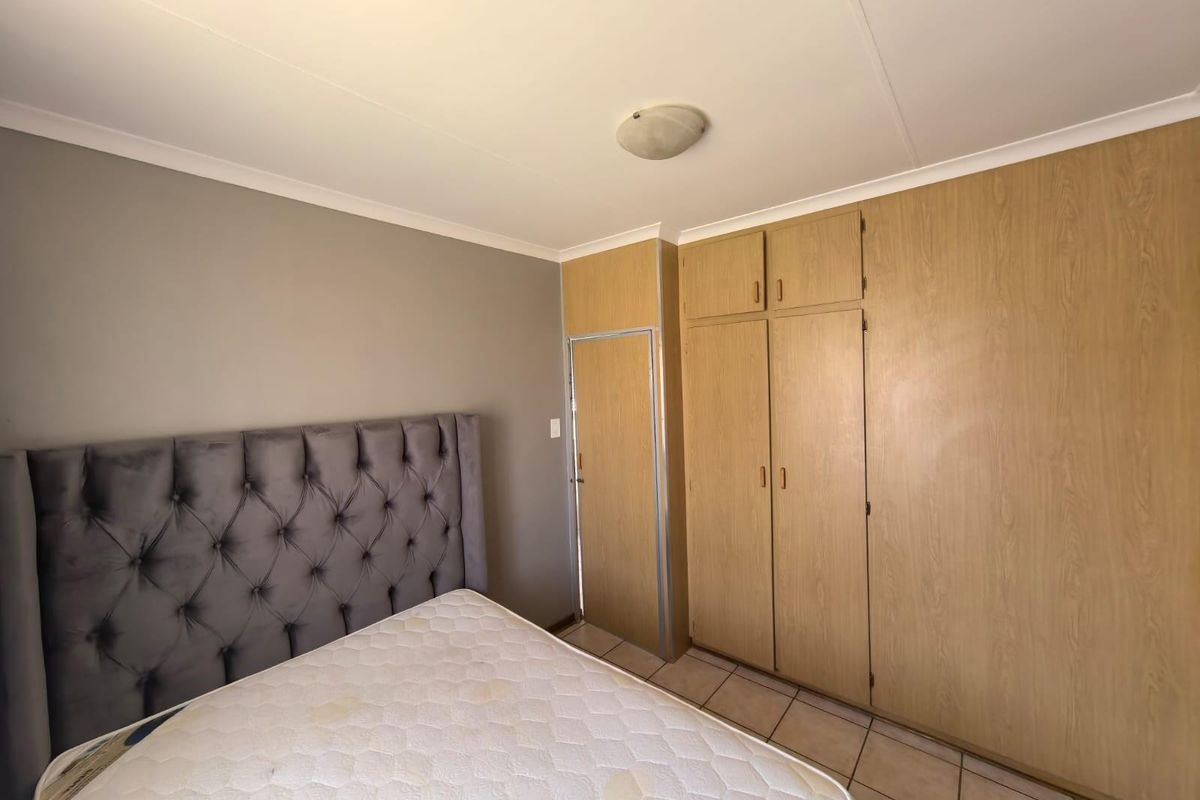 A bedroom featuring built-in wooden cupboards and tiled flooring, providing functional storage space.