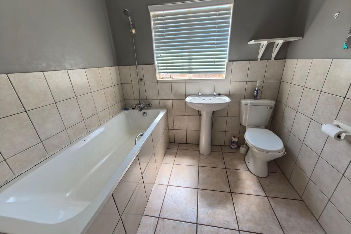 A functional bathroom featuring a bathtub with shower attachment, pedestal basin, and toilet, finished with neutral wall and floor tiling.