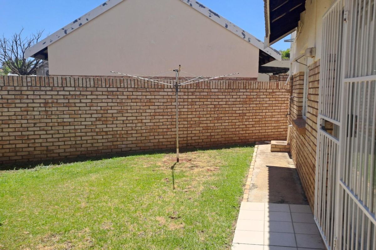 A private rear garden featuring a brick boundary wall, a small lawn area, and a paved walkway adjacent to the house exterior.