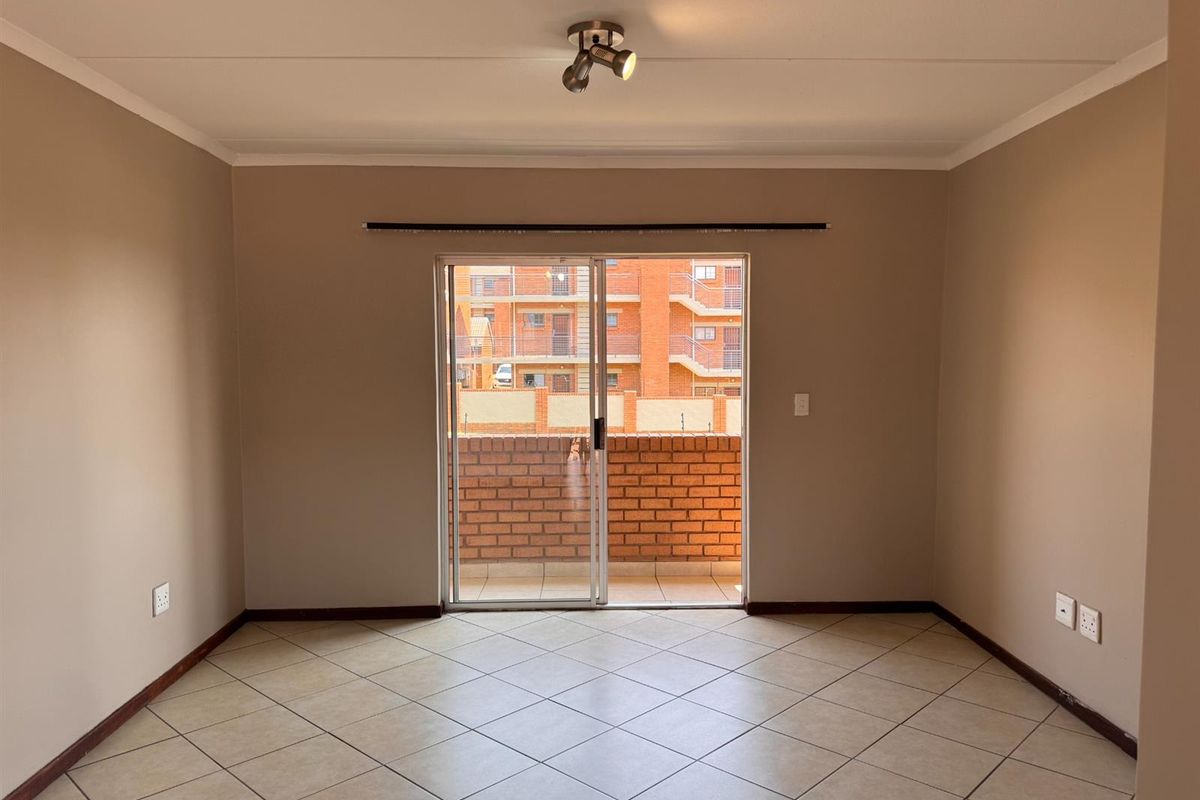 A bright, empty living room featuring neutral tiled flooring, coved ceilings, and a sliding glass door providing access to an outdoor balcony area.