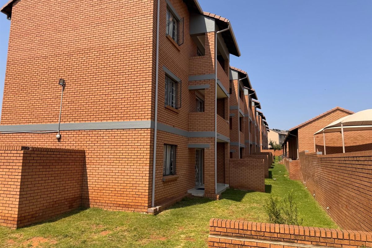 Rear view of a multi-story apartment complex featuring face brick construction, private ground-level access, and a shared lawn area.