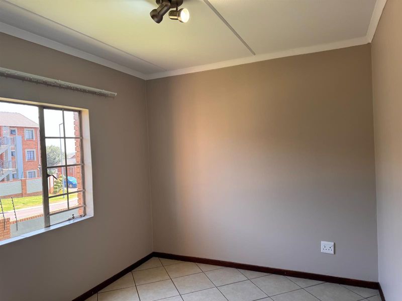 A clean, empty bedroom featuring neutral wall paint, tiled flooring, and a window with security bars, offering a blank canvas for personalization.