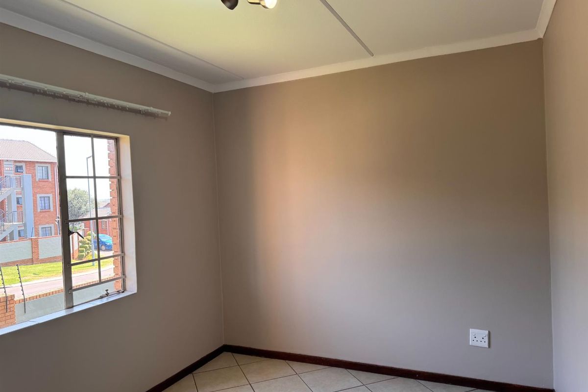 A clean, empty bedroom featuring neutral wall paint, tiled flooring, and a window with security bars, offering a blank canvas for personalization.