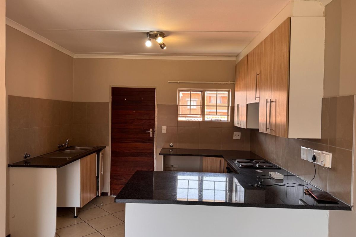 A functional kitchen featuring granite countertops, built-in cabinetry, an electric hob, and tiled finishes, offering a clean and practical workspace.