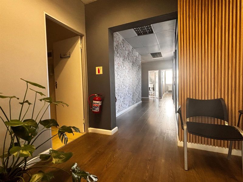 A well-maintained office hallway featuring dark laminate flooring, decorative wallpaper, timber slat wall accents, and a suspended ceiling with integrated lighting.
