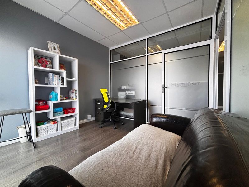 A professional office space featuring laminate flooring, a suspended ceiling with integrated lighting, and a modern frosted glass partition wall.