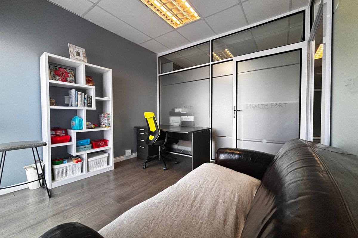 A professional office space featuring laminate flooring, a suspended ceiling with integrated lighting, and a modern frosted glass partition wall.