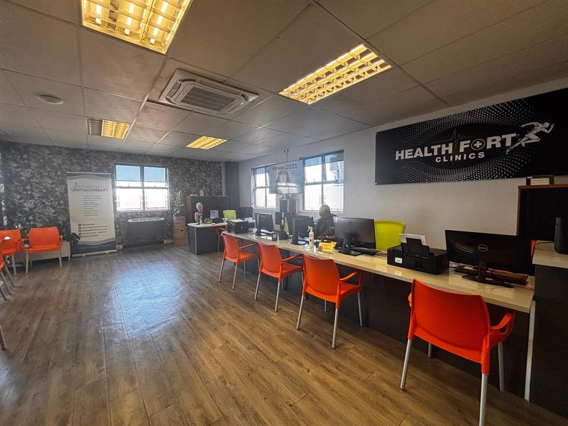 A functional office space featuring laminate wood flooring, recessed fluorescent lighting, a ceiling-mounted air conditioning unit, and a long built-in reception desk.