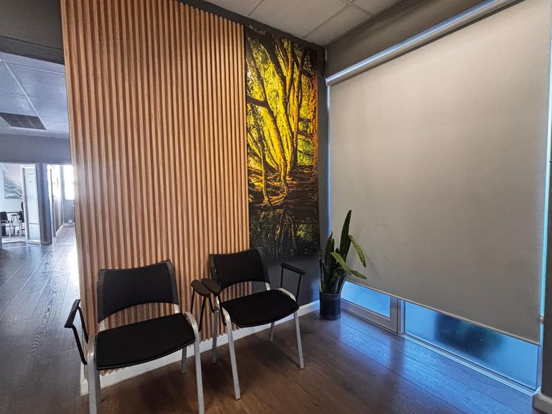 A modern office waiting area featuring decorative timber slat wall paneling, laminate flooring, and a large roller blind for privacy.