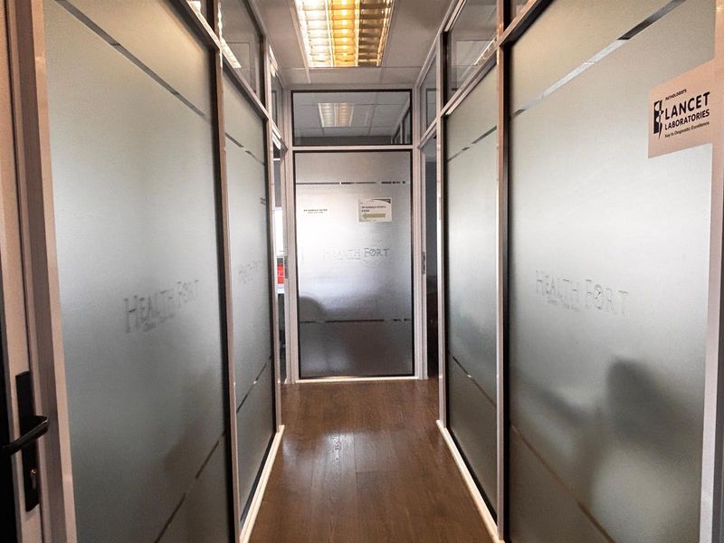 A professional office hallway featuring modern frosted glass partitions, laminate flooring, and recessed ceiling lighting, creating a clean and organized workspace environment.