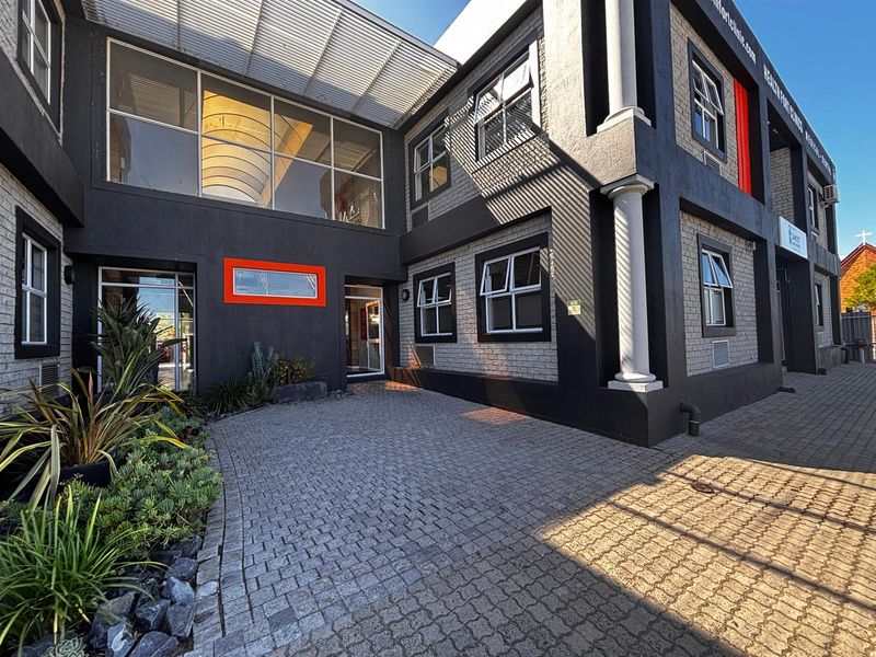 Modern office building exterior featuring a paved entrance, architectural columns, and large glass windows with a contemporary dark and light brick facade.