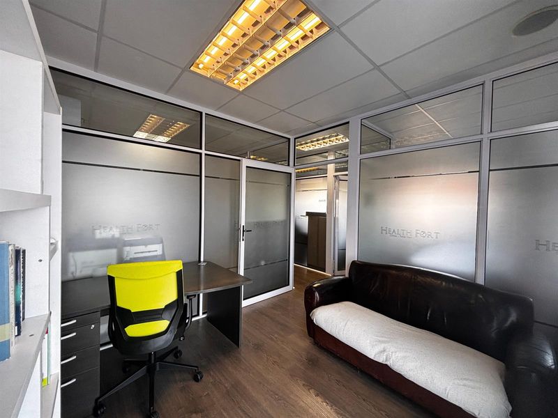 A professional office space featuring frosted glass partitions, suspended ceiling with integrated lighting, and durable laminate flooring.
