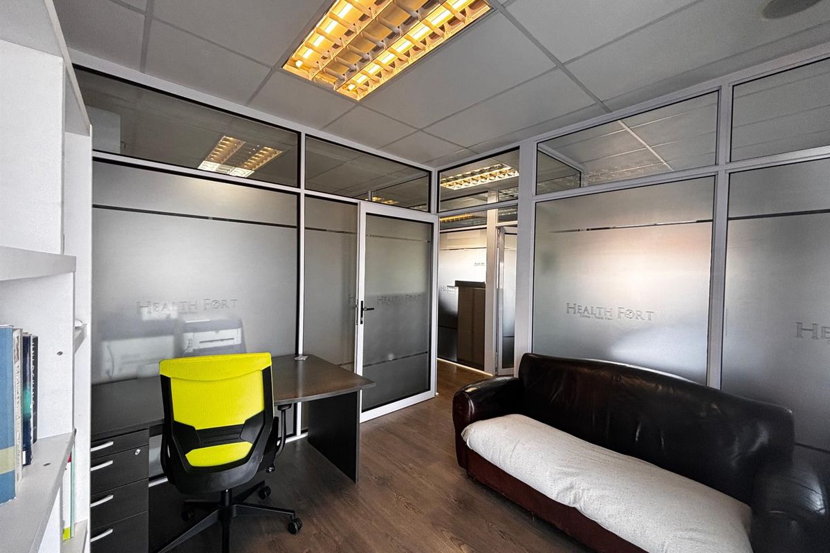 A professional office space featuring frosted glass partitions, suspended ceiling with integrated lighting, and durable laminate flooring.