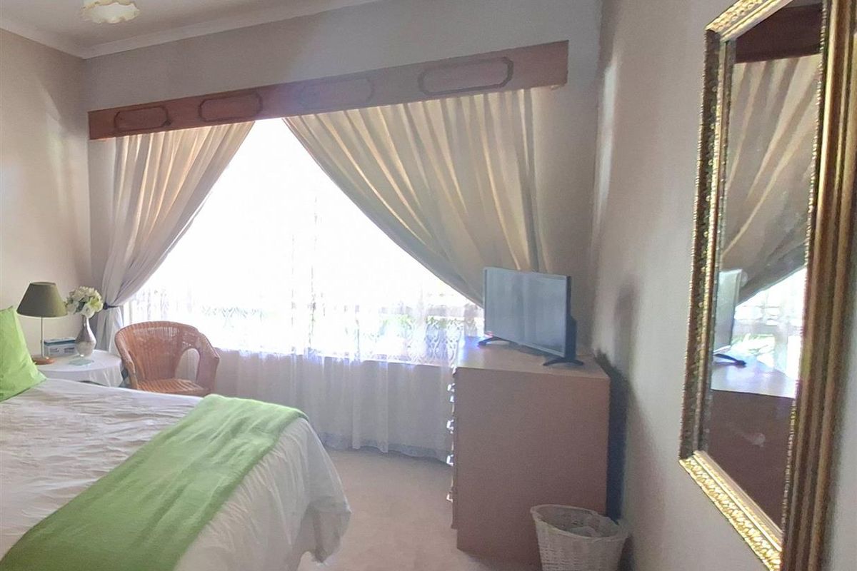 A bedroom featuring carpeted flooring, a large window with curtain pelmet, and a central light fixture.