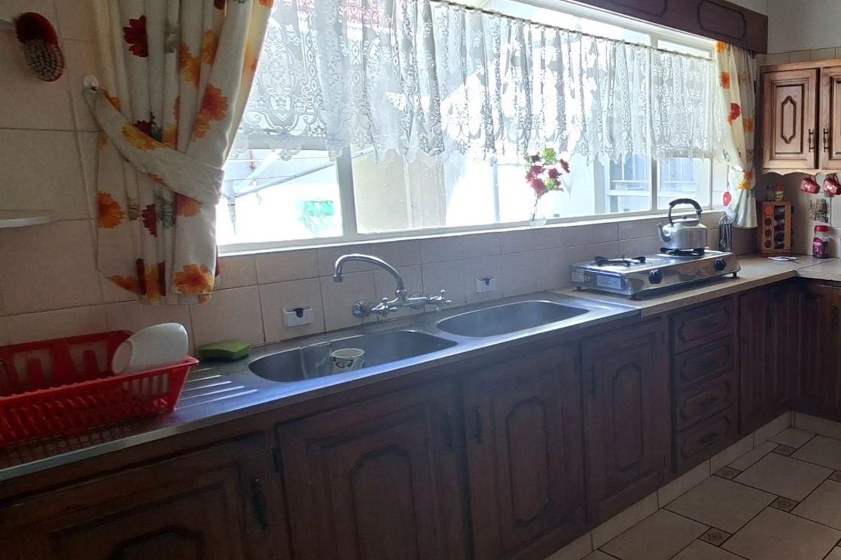 A functional kitchen featuring traditional timber cabinetry, a double stainless steel sink, tiled splashbacks, and ceramic floor tiles.