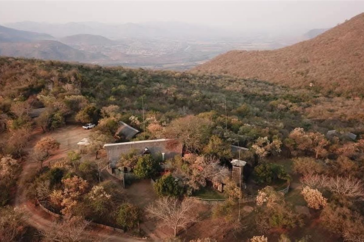 Aerial view of a farm property nestled in a mountainous landscape, featuring multiple structures with thatched roofing surrounded by natural vegetation.