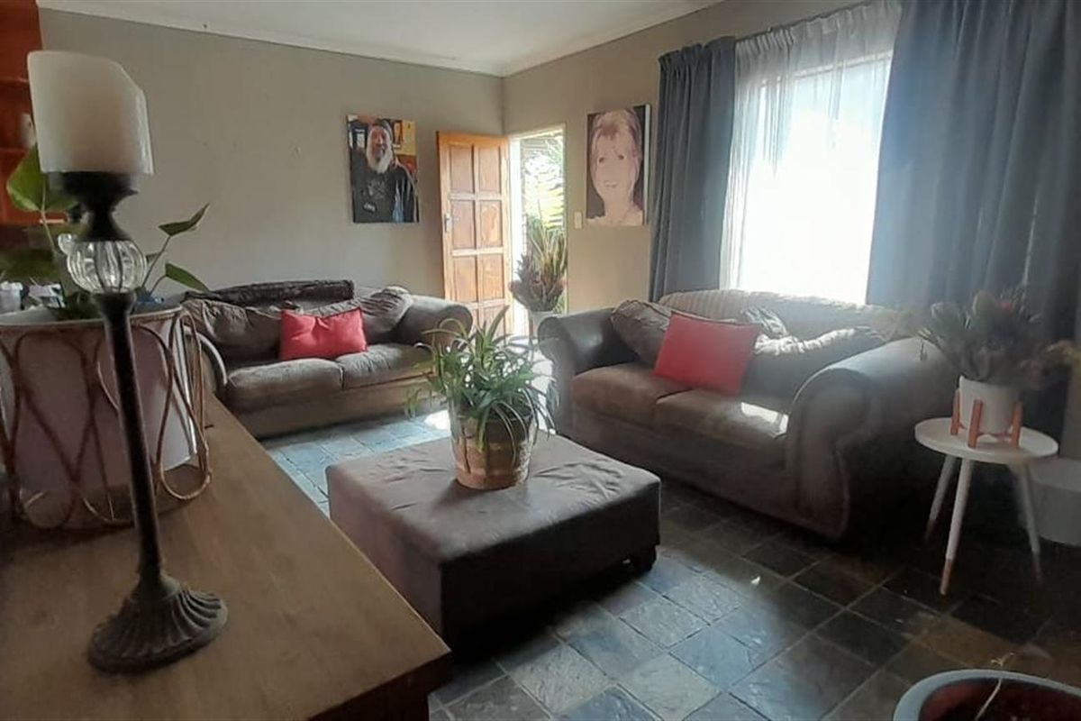 A living room featuring dark tiled flooring, natural light through a window, and direct access to an exterior door.