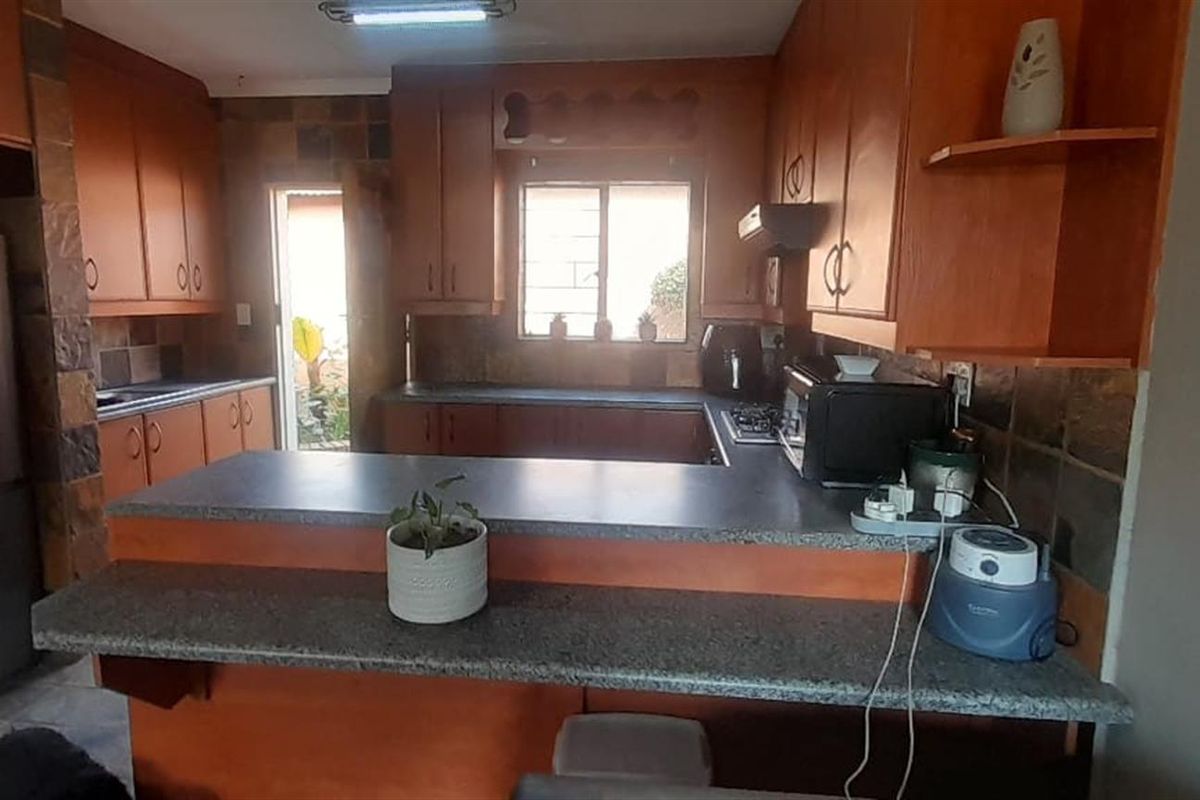 A functional kitchen featuring wooden cabinetry, stone tile backsplash, laminate countertops, and a breakfast bar, providing a practical layout for daily meal preparation.