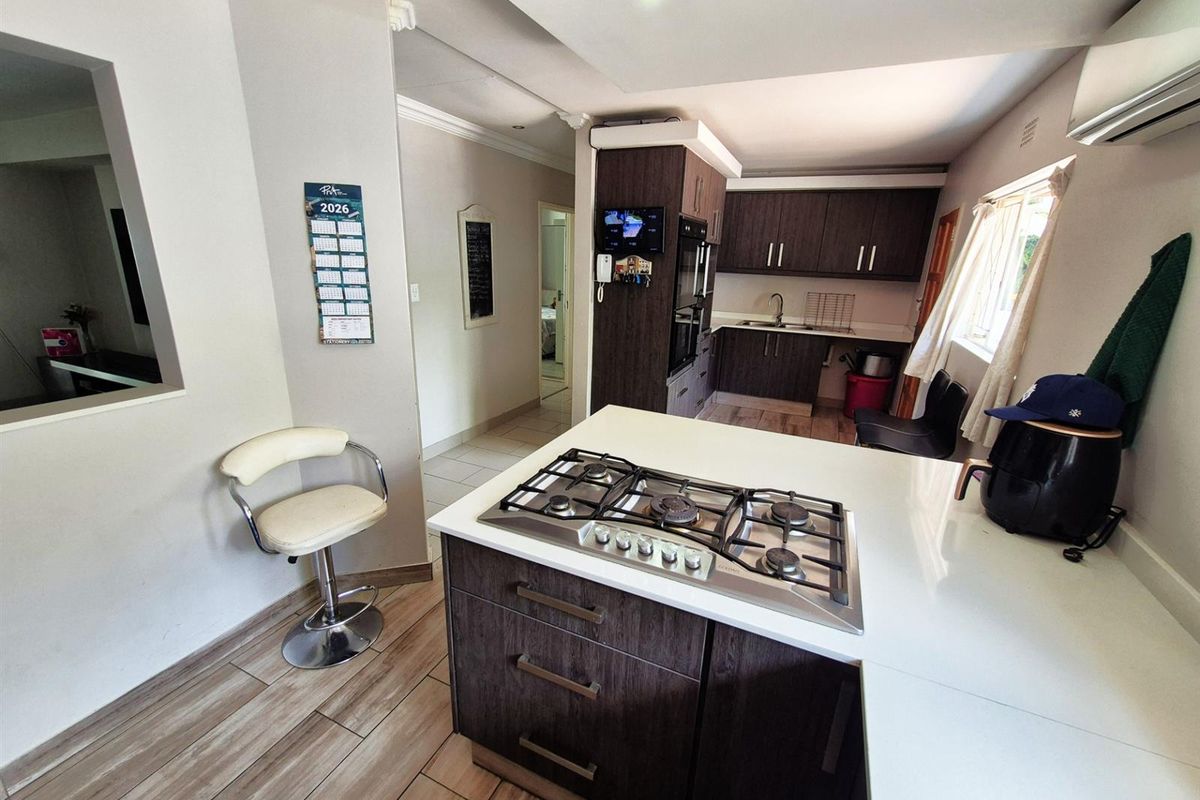 Modern kitchen featuring a central island with a built-in gas hob, dark wood cabinetry, and light-toned tiled flooring.