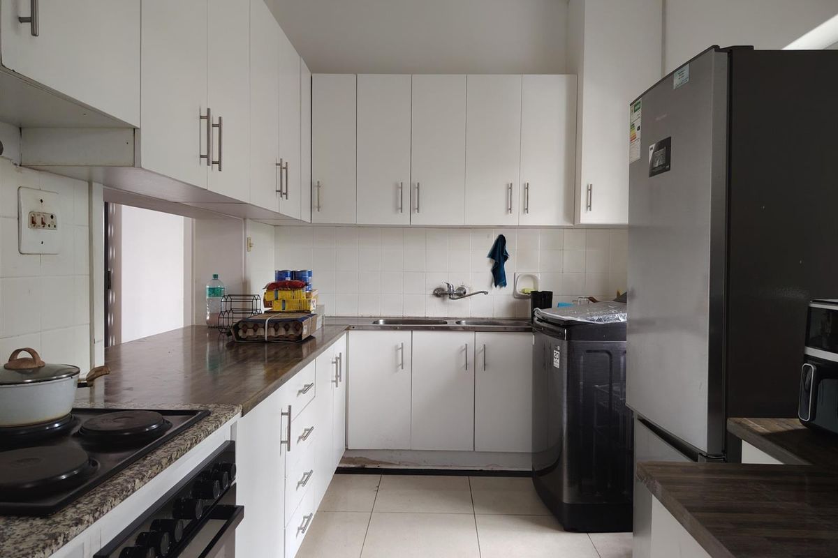 A functional kitchen featuring white cabinetry, dark laminate countertops, a built-in stove, and tiled flooring, offering a clean and practical workspace.