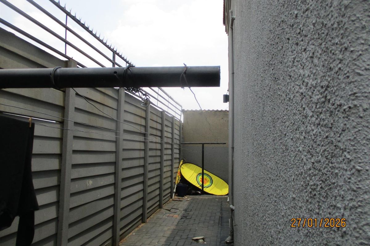 A narrow side passage featuring paved flooring, a precast concrete boundary wall with security spikes, and external plumbing fixtures.