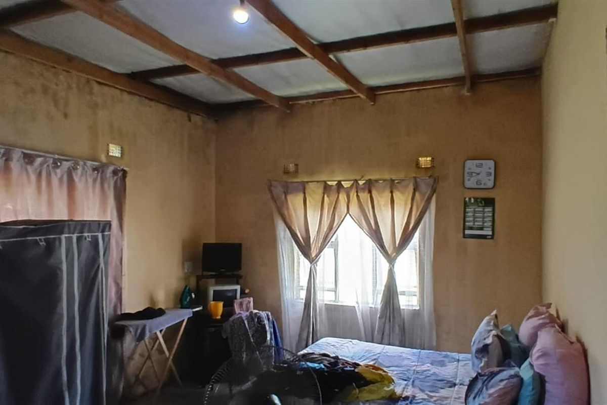 A bedroom featuring exposed timber ceiling beams and natural light through windows, requiring cosmetic updates to improve the overall finish and condition.