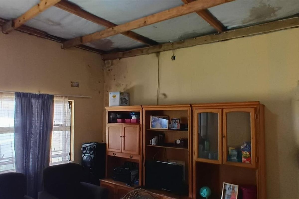 A living room featuring exposed timber ceiling beams and visible wall damage, requiring maintenance and cosmetic updates to improve the interior condition.