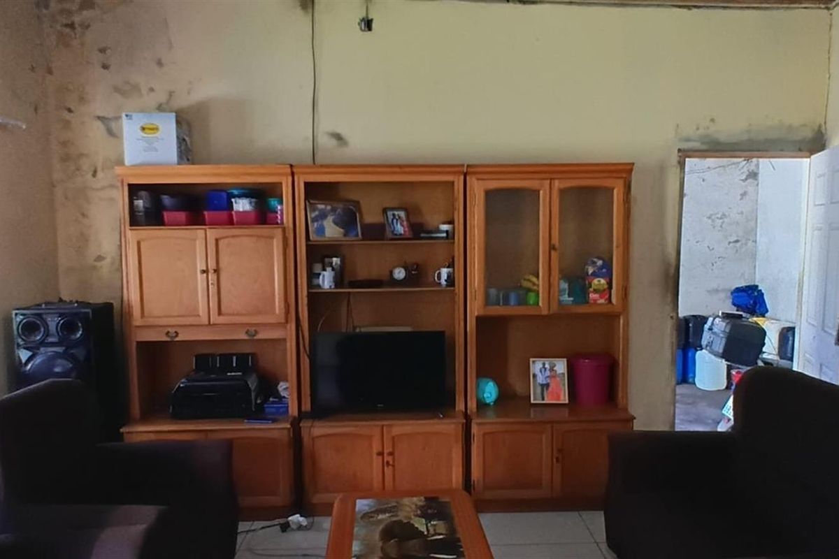 A living room featuring built-in wooden cabinetry and tiled flooring, showing signs of significant wall deterioration and moisture damage.