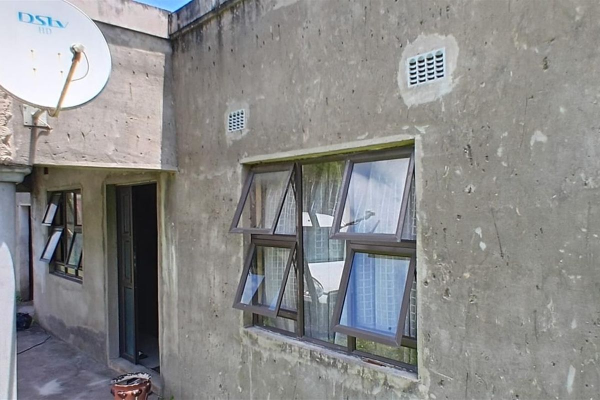 Exterior view of the property featuring an unfinished concrete facade, aluminium window frames, and a satellite dish installation.