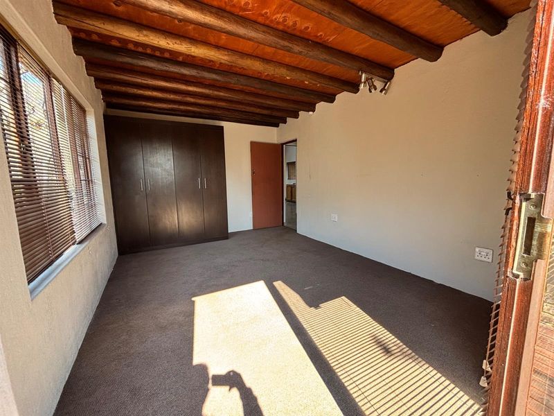 A vacant bedroom featuring exposed timber ceiling beams, built-in cupboards, and carpeted flooring, offering a neutral space ready for personalization.
