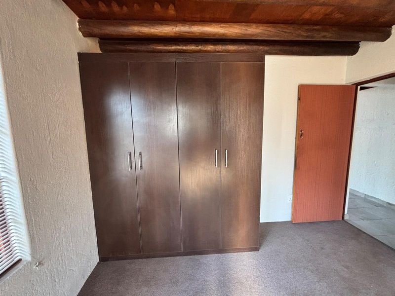 A bedroom featuring built-in wooden wardrobes, exposed timber ceiling beams, and carpeted flooring.