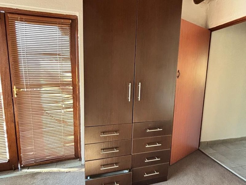 Bedroom featuring exposed timber ceiling beams, a built-in wardrobe with integrated drawers, and a glass panel door with venetian blinds.
