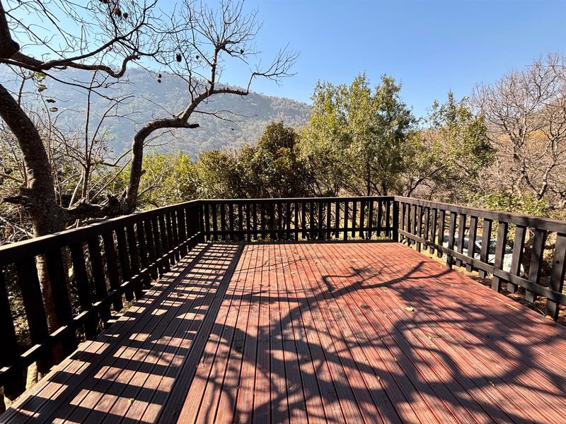 An elevated timber deck featuring a wooden balustrade, offering scenic views of the surrounding trees and mountain landscape.