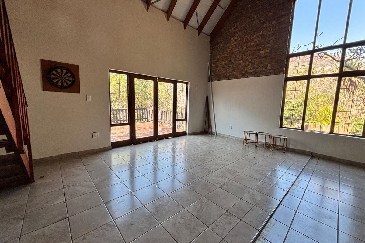 Spacious living area featuring a vaulted ceiling with exposed timber rafters, a brick feature wall, tiled floors, and large windows leading to a deck.