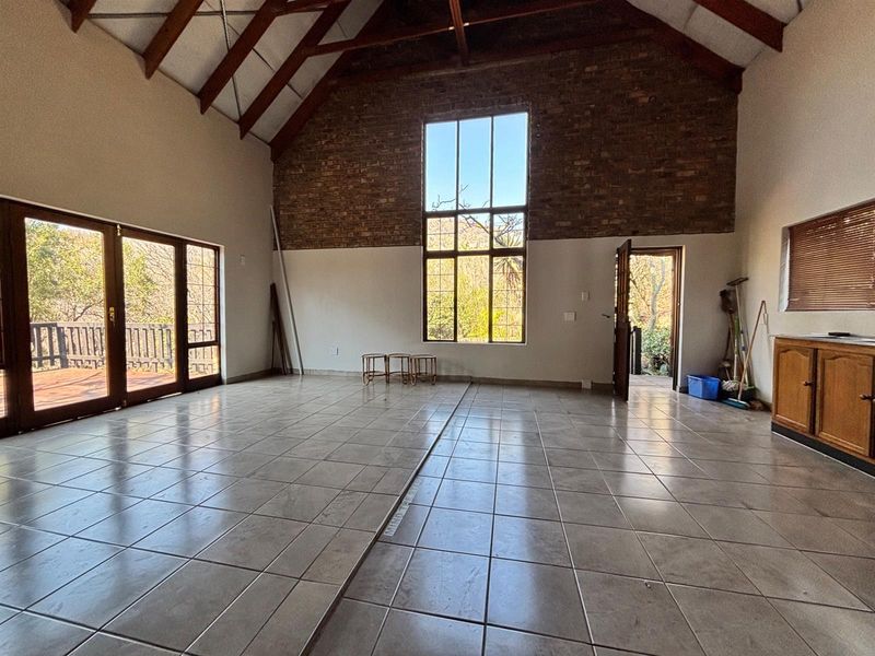 Spacious living area featuring high vaulted ceilings with exposed timber trusses, an exposed brick wall, large windows, and direct access to an outdoor deck.
