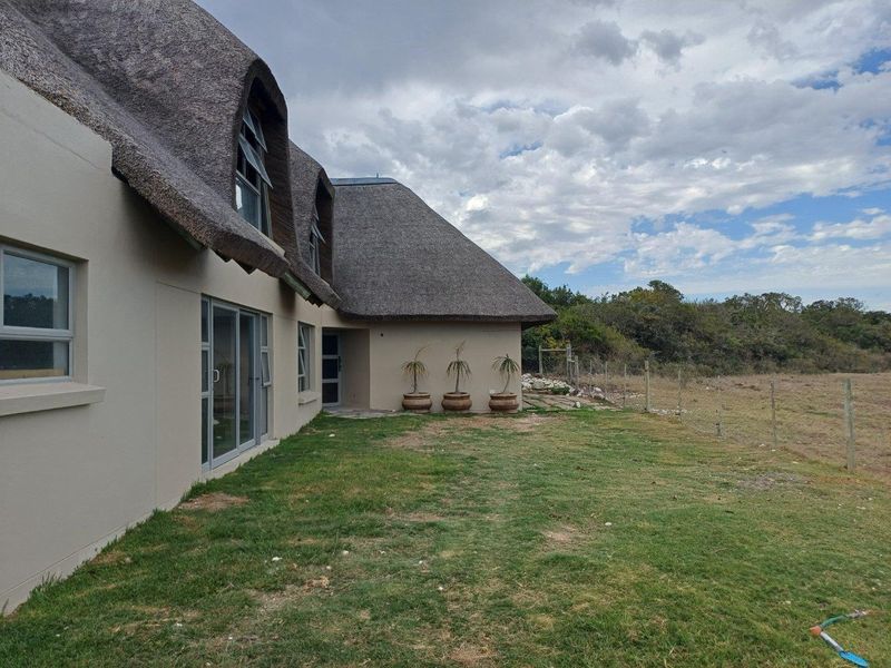 A view of the rear exterior of the house, featuring a traditional thatched roof, sliding glass doors, and a grass lawn.